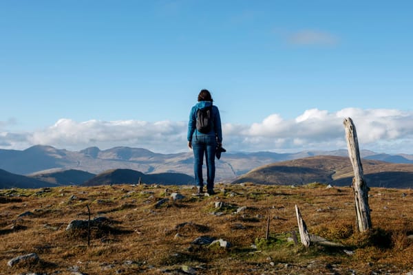 A colour photograph of a woman looking out over hills from the top of a hill. 