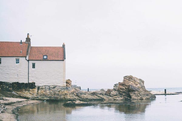 A white building with an orange roof sits behind some rocks o